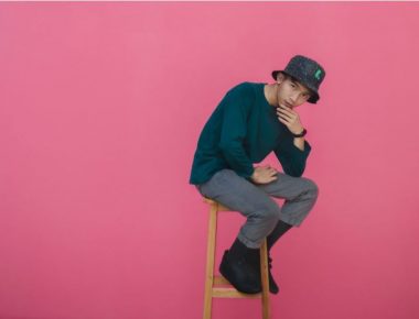 Young man sitting on a stool with a pink background