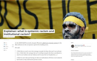 Screenshot showing an Aboriginal man with a yellow headband in front of a yellow protest banner