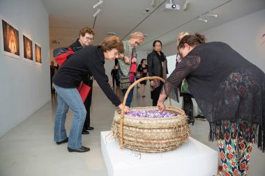 This image illustrates people hunched over a basket artwork in a gallery space, there is a welcoming and inviting sense - and also a sense of curiousity too