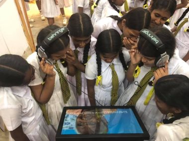 School girls look at a screen display' two are wearing headphones