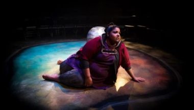 shot from the theatre production of 'bug' showing a woman of colour sitting on a smooth grey stage