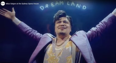 Image of an Opera Australia cast member with arms spread wide under a 'DREAMLAND' sign