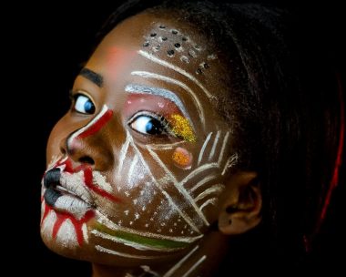 A young black woman with coloured makeup all over her face and shoulders