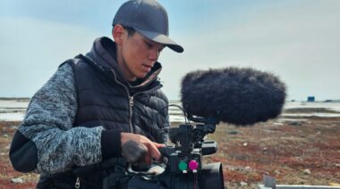 A young Inuit man operates a video camera outdoors